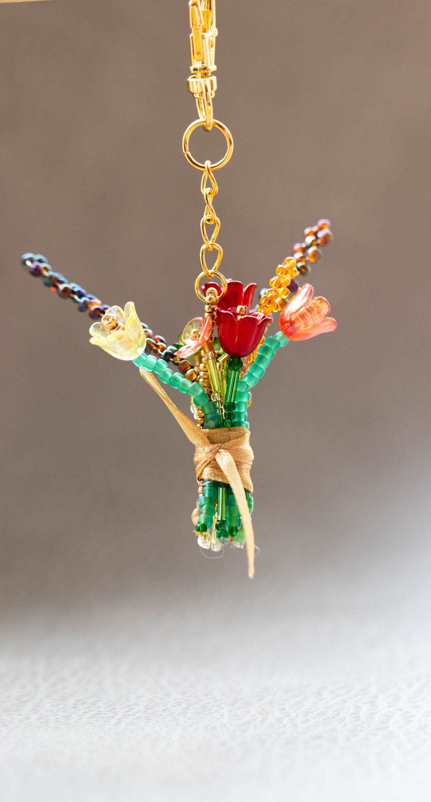 Colorful flower-shaped keychain with gold chain on a neutral background