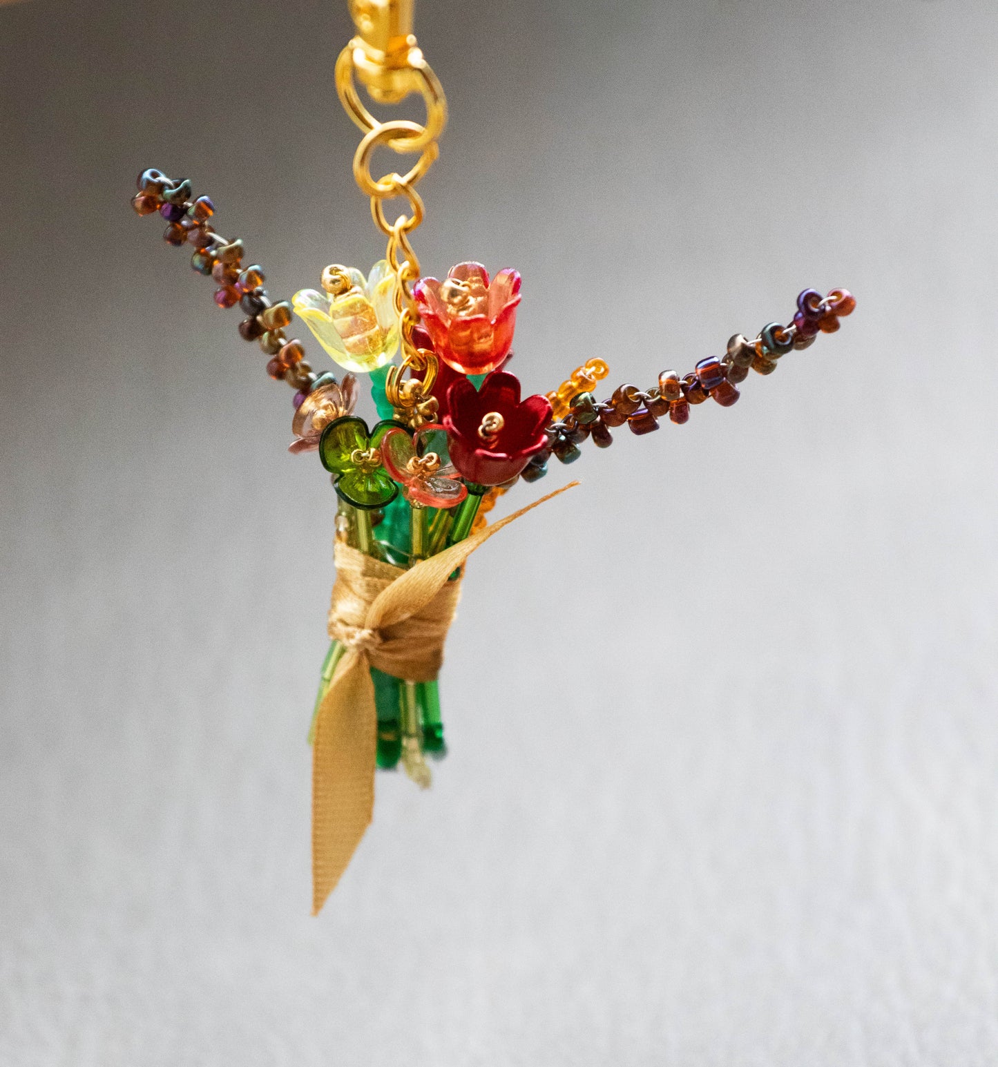Colorful glass flower bouquet charm on a gold chain against a gray background
