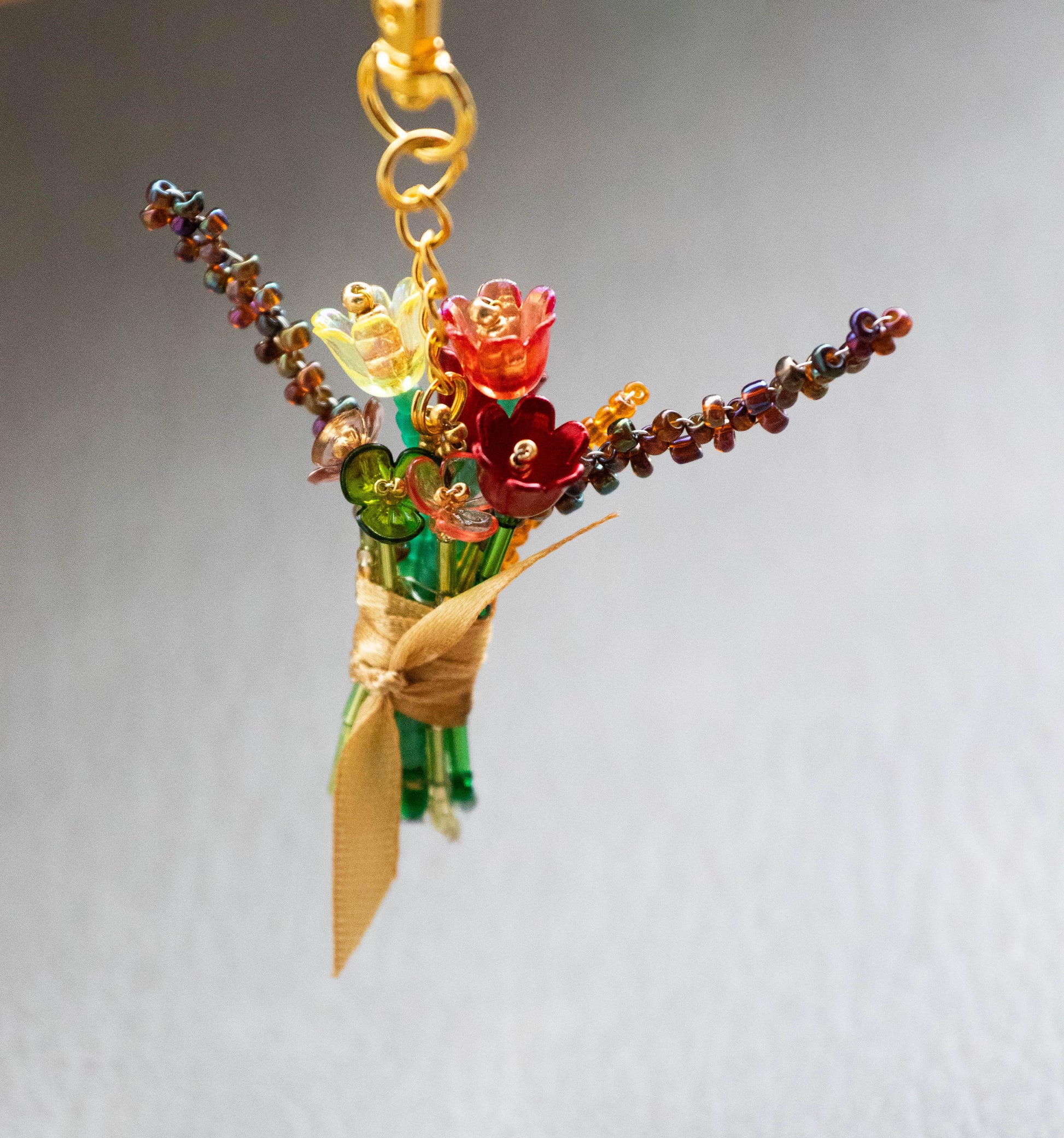 Colorful glass flower bouquet charm on a gold chain against a gray background