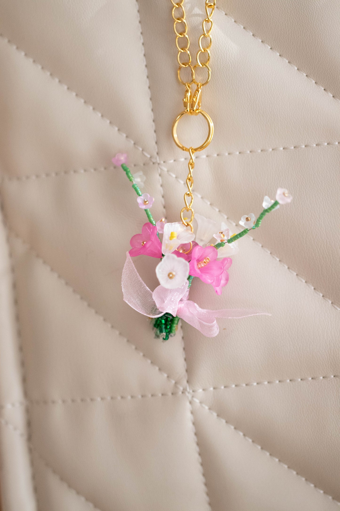 Floral keychain with pink flowers and green leaves on a beige quilted background