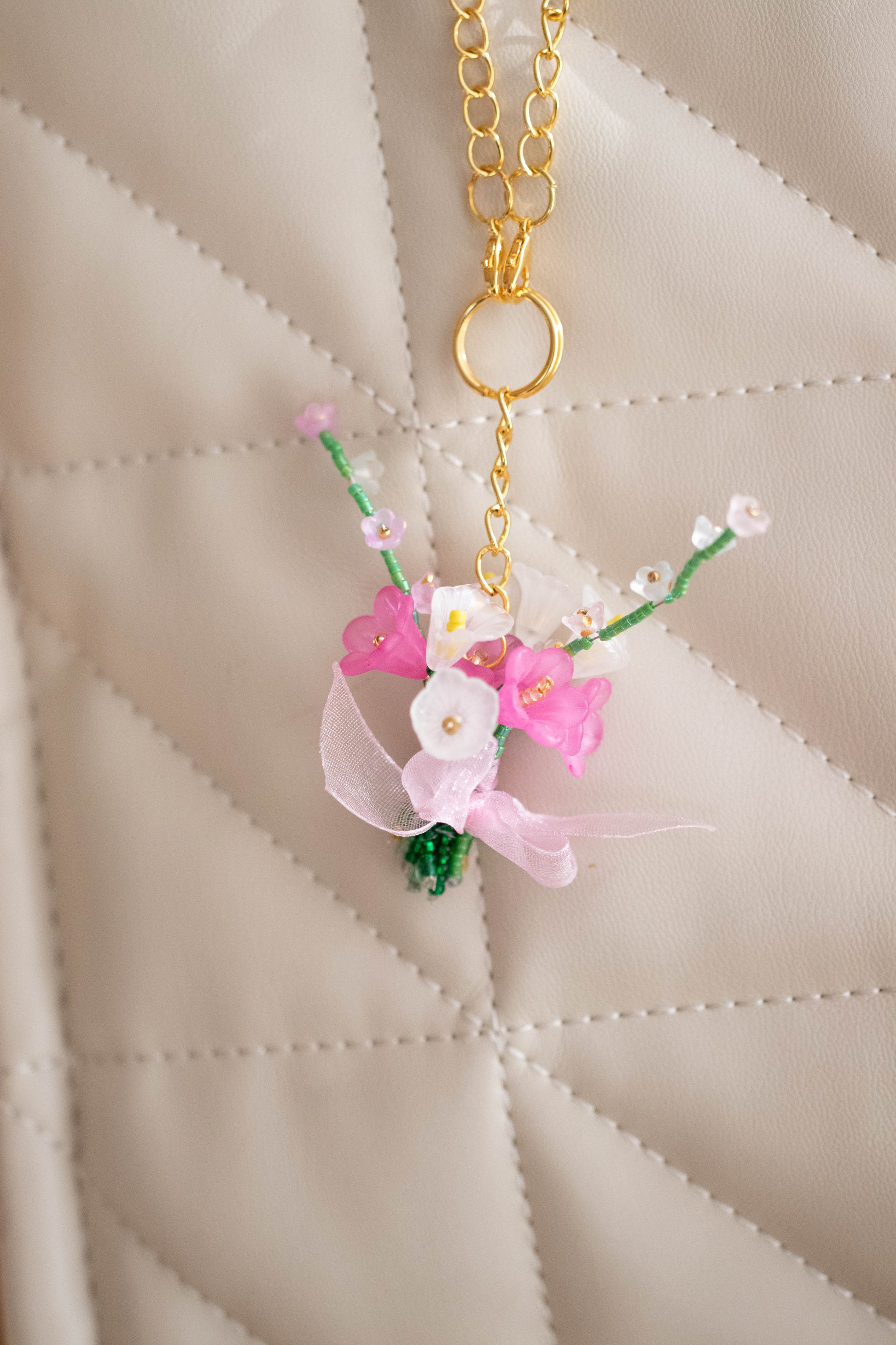 Floral keychain with pink flowers and green leaves on a beige quilted background
