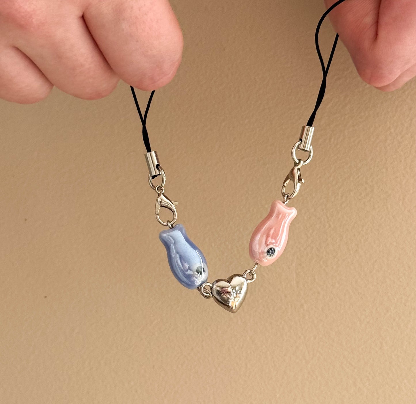 Two phone charm straps with fish and heart designs on a beige background