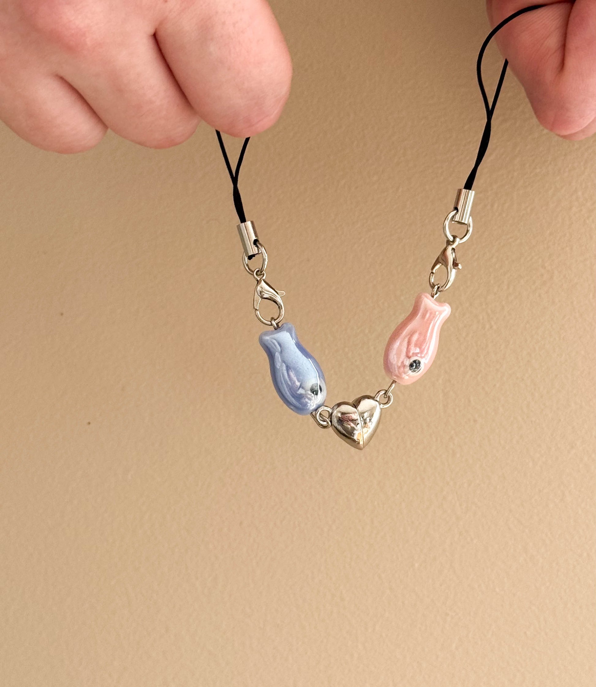 Phone charm with blue and pink fish and a heart on a beige background